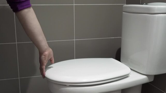 Hand closes or opens the toilet lid a bathroom toilet.
