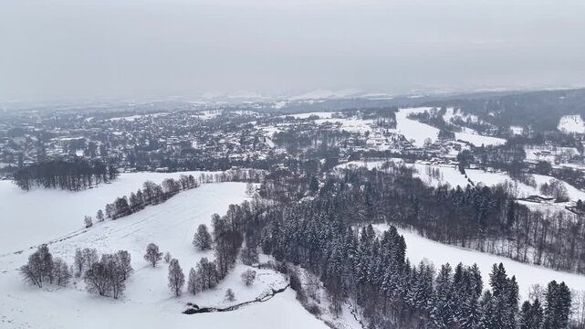 Snowy aerial view of rolling countryside with frosted fields and dark evergreen forest, drone surveyor mapping