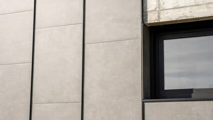 Fototapeta premium Wall cladding tiles made of light grey ceramic material surround a modern window frame in a minimalist building design.