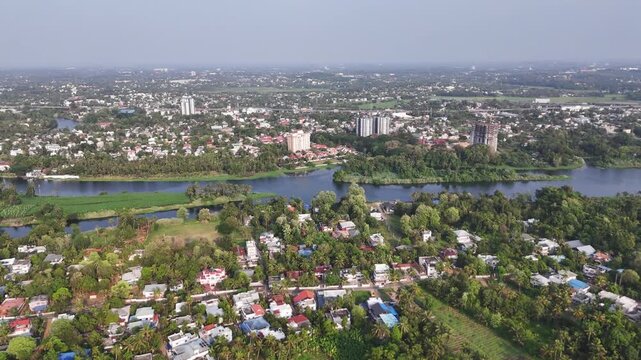 Cinematic aerial view of Aluva showcasing the winding Periyar River flowing through lush tropical landscapes, riverside communities, and modern residential developments stretching across the horizon.