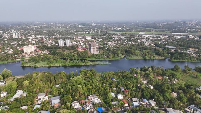 Cinematic aerial view of Aluva showcasing the serene waters of the Periyar River flowing through lush tropical landscapes, residential neighborhoods, and emerging urban developments beneath clear ski