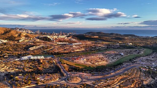 Sunset aerial urban expansion with skyline, drone sweep revealing housing, road network and golfcourse,
