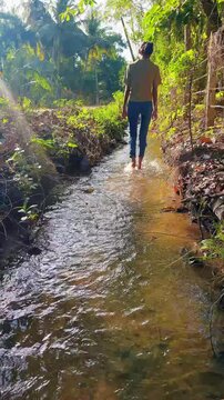 Slow motion footage of a young woman walking barefoot through a shallow natural canal, emphasizing mindfulness, tactile sensation, relaxation and connection with nature.