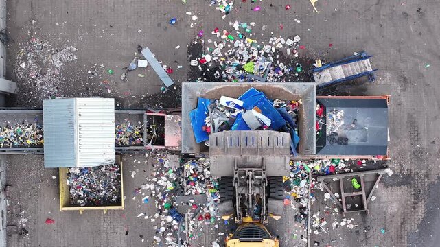 Plastic waste is loaded into a truck at a recycling facility. Sorting equipment separates materials. Bins contain different types of plastic. The area is organized for efficient waste management.