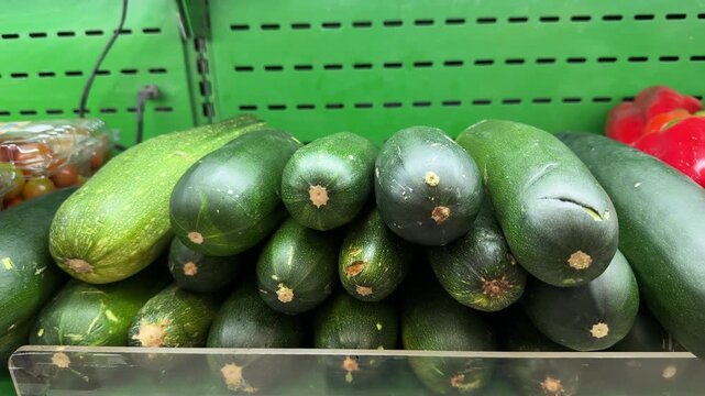 Zucchini squash are stacked in a neat pile on a green supermarket shelf under bright indoor lighting, useful for nutrition, diet or grocery shopping themes.