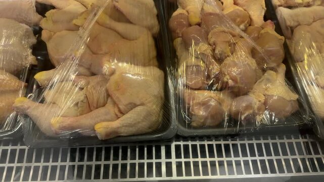 Mixed poultry legs and drumsticks rest on plastic trays under cling film in a refrigerated supermarket display, useful for themes of grocery shopping and meat consumption.