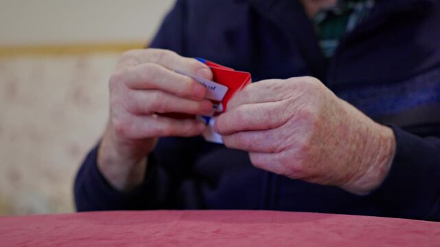 Senior player carefully reviews and selects playing cards while concealing their hand from opponents during a strategy game. Highlights tactical thinking and cognitive stimulation for older adults