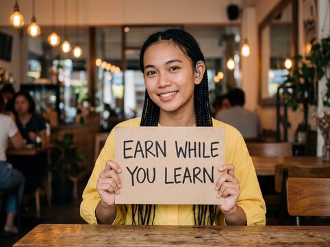 Young Southeast Asian woman with hearing aid holds earn while you learn sign smiling in cafe