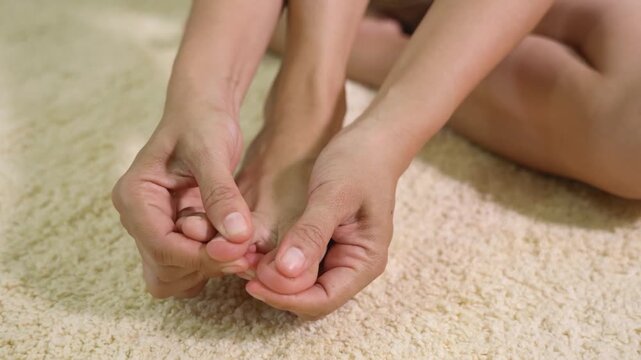 Close-up of a person holding and massaging a painful toe while sitting on the floor. Concept of foot pain, toe injury, gout, bunion, inflammation, podiatry, and foot care.
