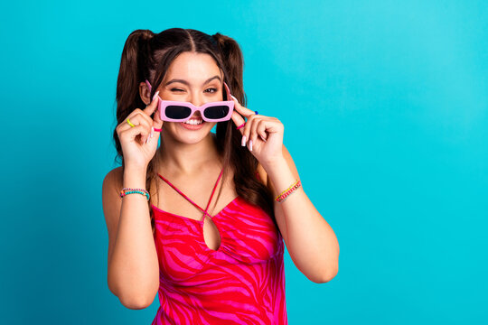 Young chic girl with pink sunglass smiles in a blue studio backdrop wearing a pink zebra swimsuit