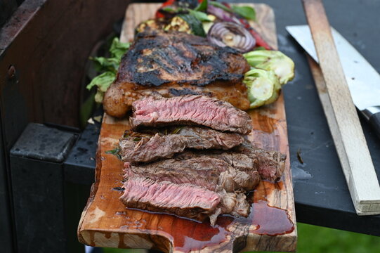 Juicy sliced grilled beef steak served on a wooden board with fresh salad, toasted bread, and grilled vegetables. The image highlights a summer barbecue feast with premium grilled meat, colorful side 