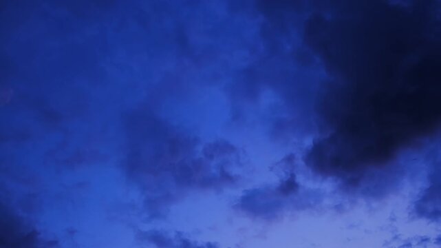 A deep dusk blue sky is filled with dense, textured clouds in varying shades of blue. Heavy cloud cover. Early morning. Before or after sunset. High quality 4k footage.