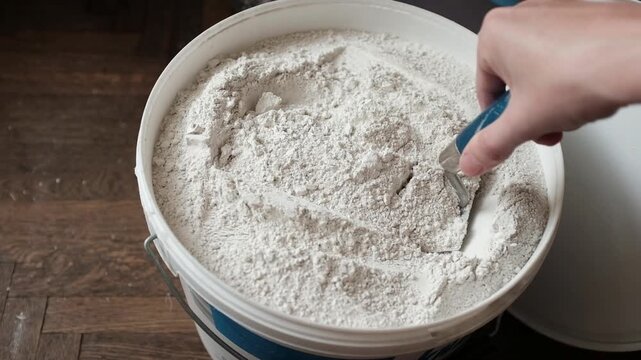 White plastic bucket filled with dry white putty or plaster powder. Home improvement, interior finishing work, construction materials, DIY repairs, and professional masonry.