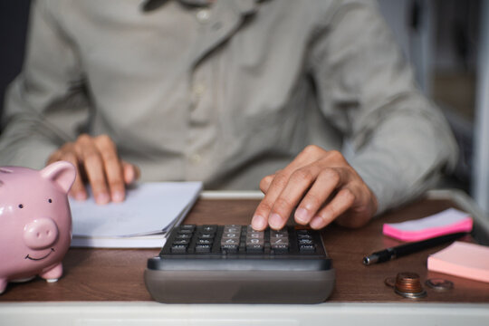 person uses calculator and writes a financial report, recording income expenses savings and deductions to manage costs and maintain an accurate budget balance.
