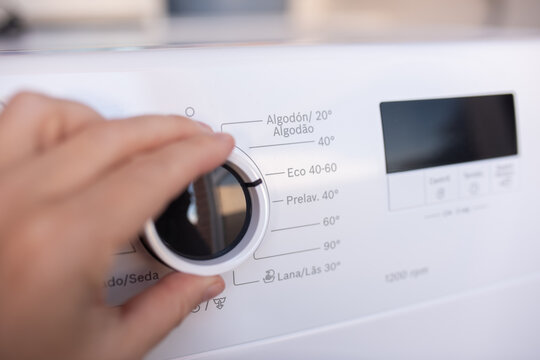 Woman hand adjusting washing machine program dial.