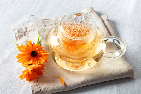 Calendula tea. Vibrant orange marigold flowers infusing in a clear glass teapot