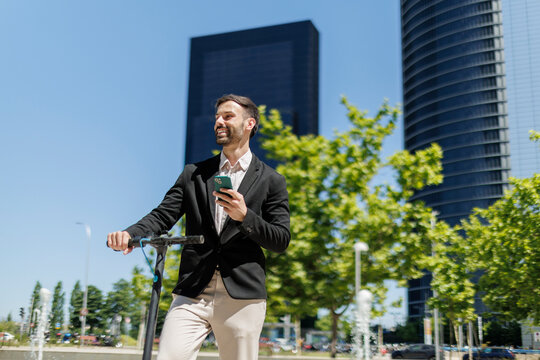 Smiling businessman using phone with electric scooter in city