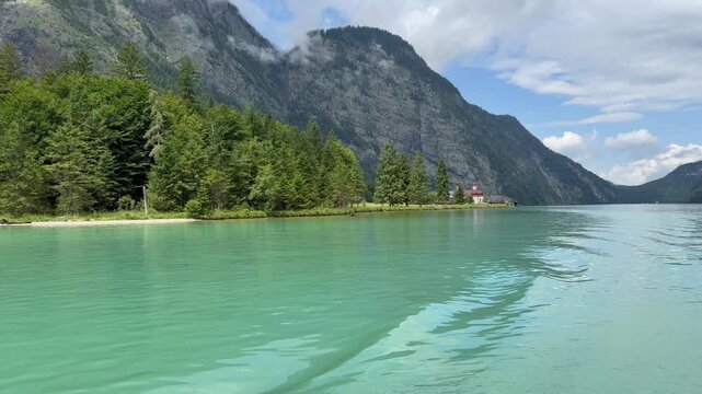 Panoramic, scenic view of Konigssee Lake. St. Bartholomew church and wooden boathouse. View from a moving boat. Konigssee, Bavaria, Germany