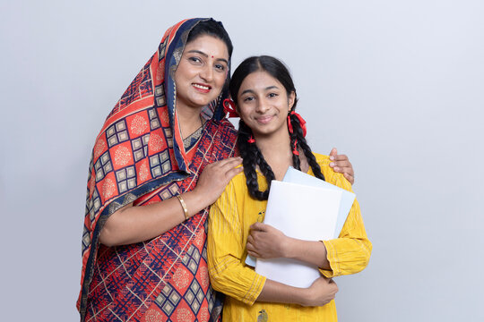 A rural Indian family of a mother and a Daughter standing with a note books in hand isolated on gray studio background. Concept of girl education in india