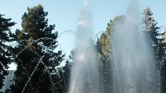 Multiple high-pressure nozzles shooting powerful streams of fresh water into the air at a public city park fountain. Summer heat, urban architecture, municipal engineering, public parks in summer.