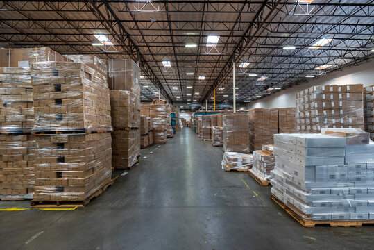Interior of a spacious and modern logistics warehouse with large quantities of cardboard boxes stacked on pallets for storage.