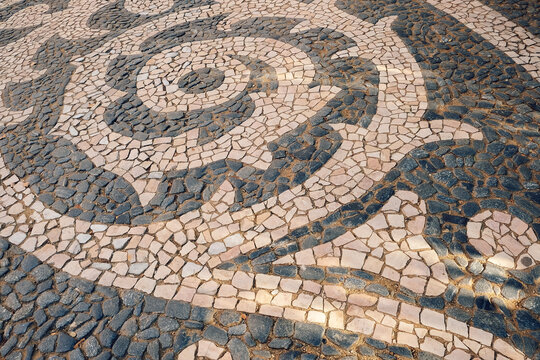 Pattern of stones on  sidewalk in  city. daylight hours showing artistic design. sidewalk features a design made of various stones arranged in curves and swirls. artwork  pavement patterns during day