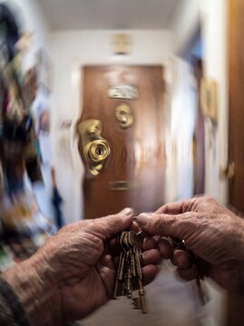 A blurry and disorienting POV shot representing Alzheimer's disease with elderly hands holding a ring of keys in front of their own front door, but the lock and the surrounding environment appear stra