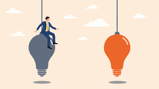 A businessman balanced on a grey light bulb with a orange bulb hanging nearby
