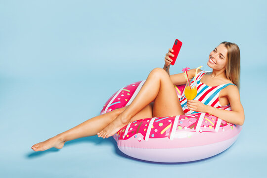 Full body young beautiful sexy woman she wear bikini swimsuit rest near hotel pool lies on rubber ring hold use mobile cell phone isolated on plain blue background Summer vacation sea sun tan concept