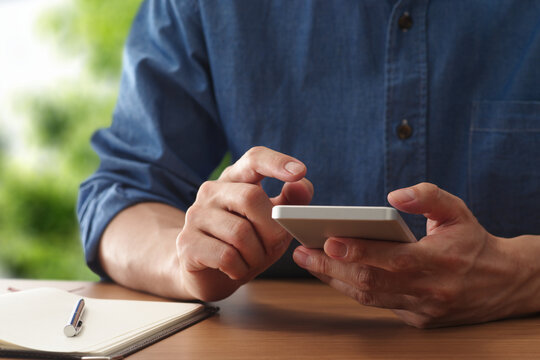 Man using smartphone app at table. Tapping mobile display.