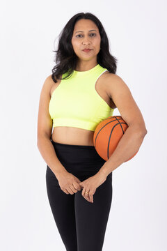 Portrait of a indian fit young woman holding basketball while looking at camera isolated on white studio background	
