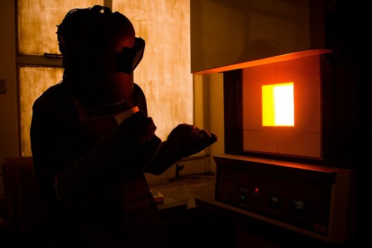A researcher opening a high temperature muffle furnace during pyrometallurgical research in a laboratory setting with glowing orange light