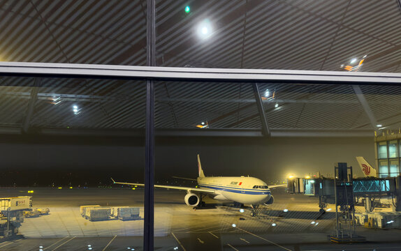 Passenger jet parked at Beijing airport terminal gate behind glass at night in China