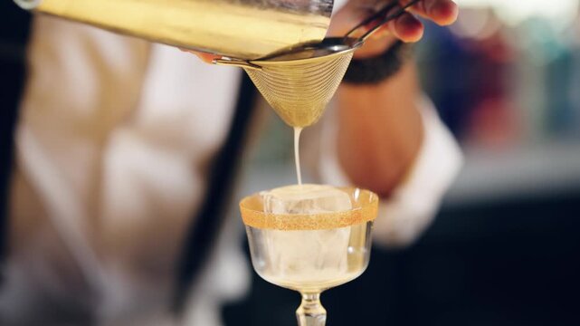 Professional mixologist preparing a sophisticated alcoholic beverage. Man pouring a creamy drink from a shaker through a strainer into a fancy glass