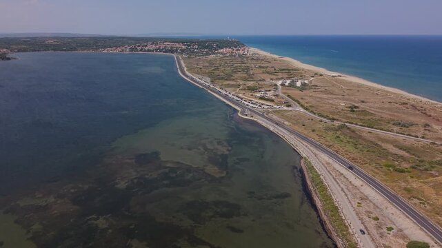 Drone scenic view of the narrow land strip separating the Etang de Leucate from the Mediterranean Sea, featuring the coastal highway, beaches, and harbor entrance canal in Occitanie, France.