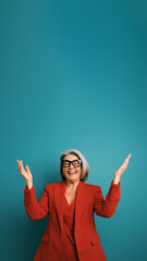 Happy senior executive woman in red pantsuit and glasses smiling, celebrating success with raised arms