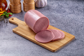 Sliced bologna sausage on wooden cutting board with spices on gray background © Andrei Starostin