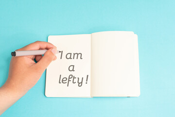 I am a lefty standing on notebook, writing with left hand, pen and table, left handed concept, handwriting a message