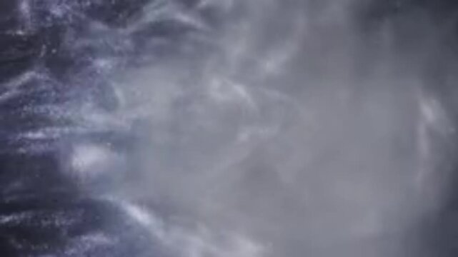 An abstract composition of fine dust particles and swirling white smoke moving dynamically against a dark background. Soft, fluid-like vortex patterns create a dramatic, mysterious,