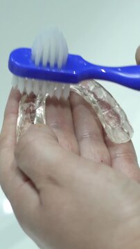 Cleaning tooth aligners.Washing and removing organic residues with a plastic toothbrush from orthodontic invisible braces.