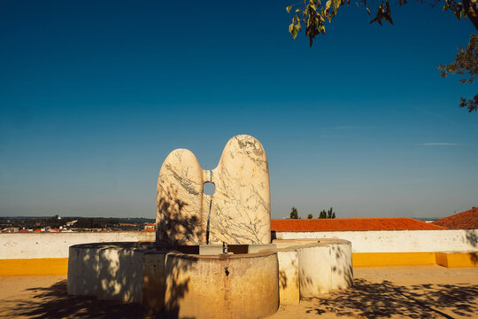 10 October 2023, Portugal, Evora - Miradouro do Jardim Diana. Font &ldquo;beijo&rdquo;, Sculpture at a viewpoint in Portugal shows two stone shapes with a hole in the center during a clear sunny day