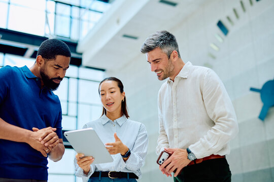 Three diverse business people discussing ideas and collaborating on a project using a tablet in a modern office