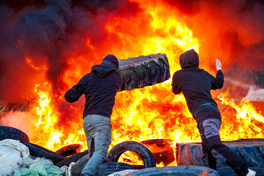 Dos personas encapuchadas junto a una barricada de neum&aacute;ticos ardiendo durante una protesta