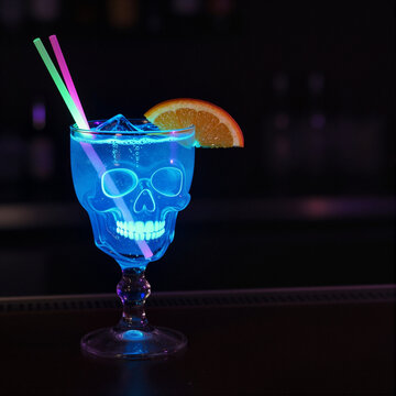 glowing cocktail in skull glass with orange slice and straws neon colors nightclub atmosphere