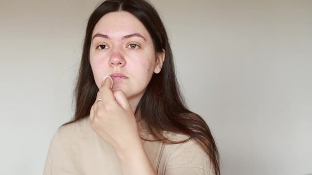 Young Caucasian woman wipes face with toner using cotton pad. Close up slow motion shows daily skincare routine. Healthy complexion and beauty care.