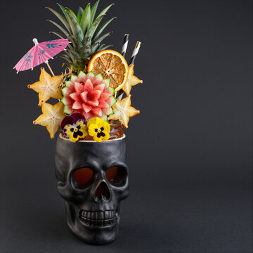 tropical cocktail with vibrant fruit garnishes in black skull glass, concept of exotic summer drinks