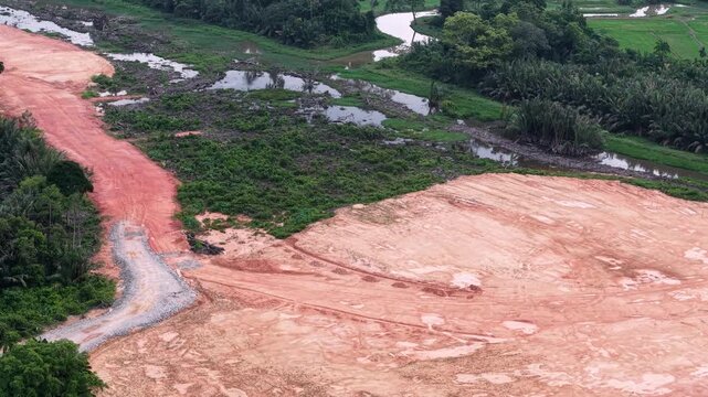 Aerial view of cleared red soil land with access road near wetland