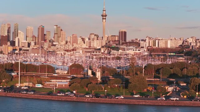 AUCKLAND, NEW ZEALAND, 27 June 2026 &ndash; A panoramic view of the Auckland skyline and Viaduct Harbour at sunset, showcasing the Sky Tower and yachts docked in the marina.