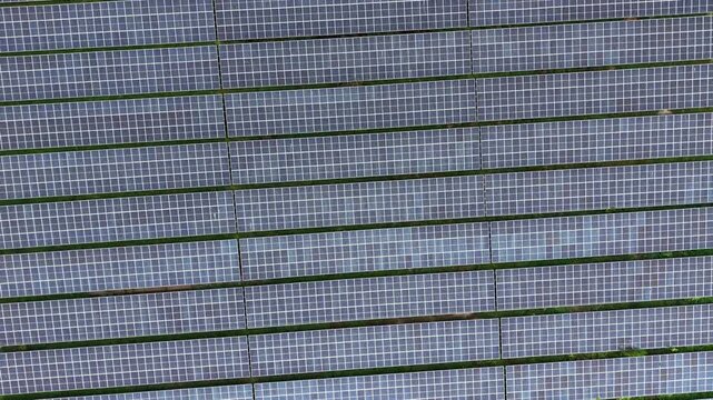 Aerial drone footage showing multiple rows of ground-mounted solar panels in a solar farm.