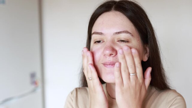 Young Caucasian woman applies serum and massages face. Close up slow motion shows skincare routine for problem skin. Healthy beauty care concept.